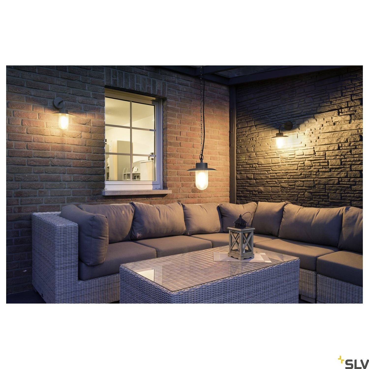 Gemütliche Terrasse bei Abenddämmerung mit Sofa und Tisch, beleuchtet von Wandlampen. Entspannte Atmosphäre für Abendgespräche.