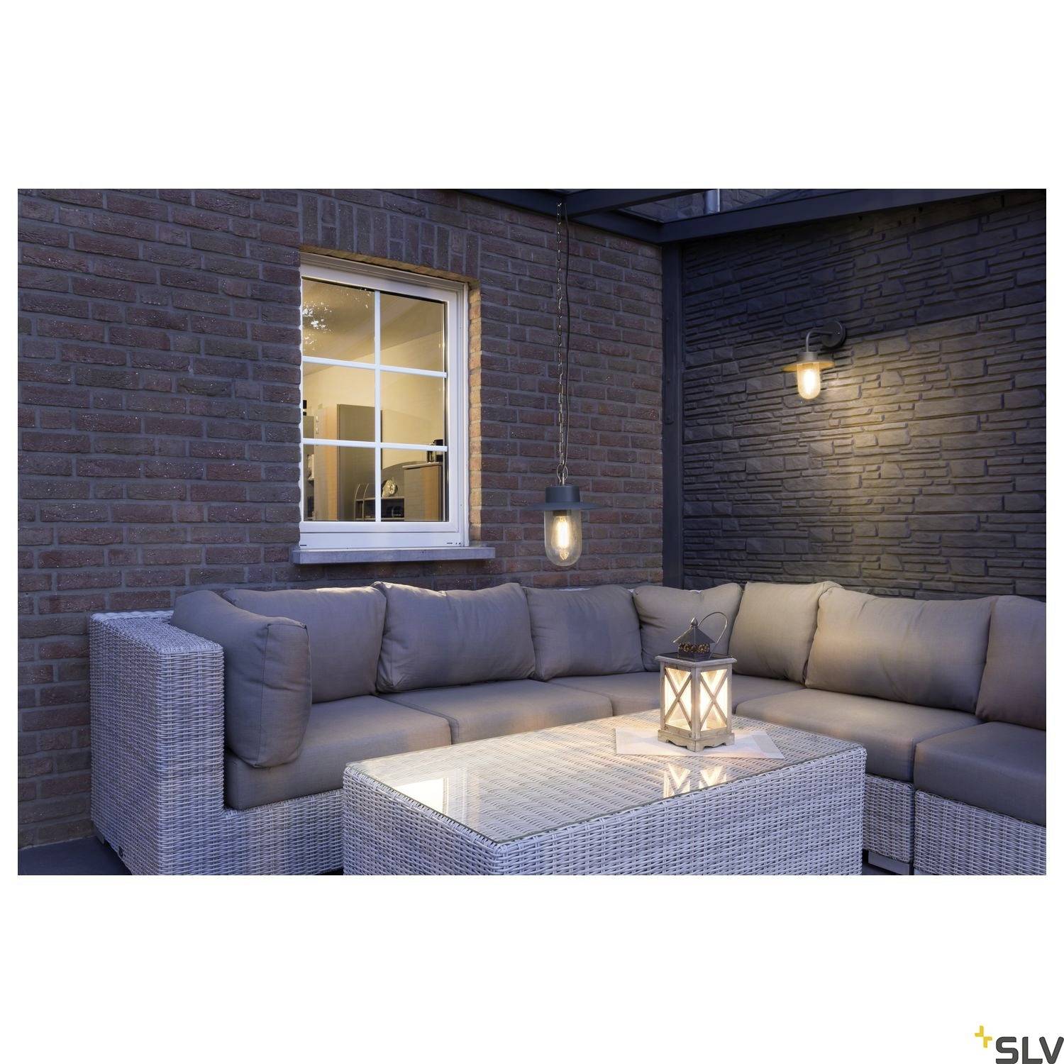 Ecksofa mit weißen Kissen auf einer Terrasse, beleuchtet von zwei Wandleuchten; Laterne auf dem Glastisch in der Mitte.