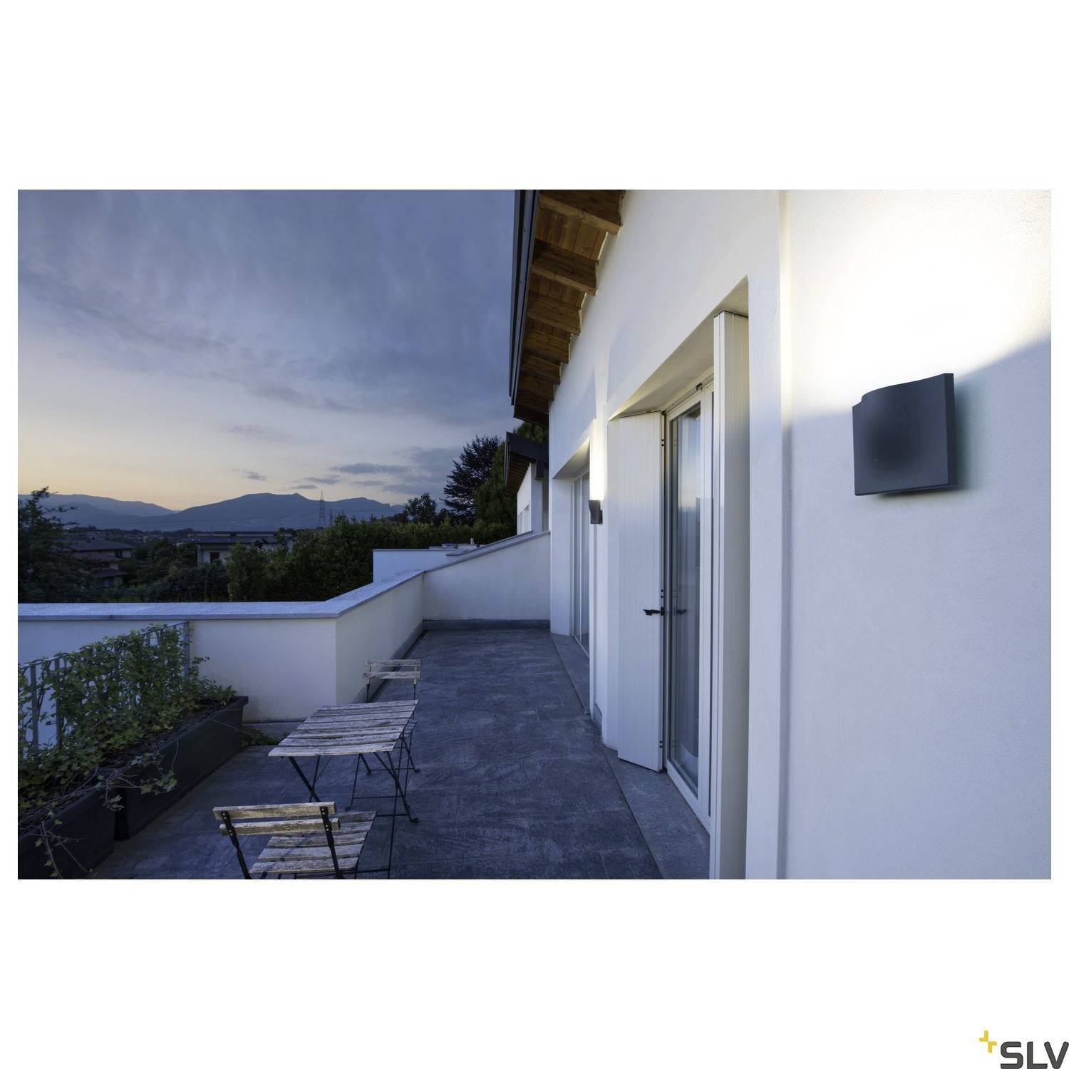 Ein Balkon mit Tischen und Stühlen bei Sonnenaufgang. Im Hintergrund sind Berge und der Morgenhimmel zu sehen.