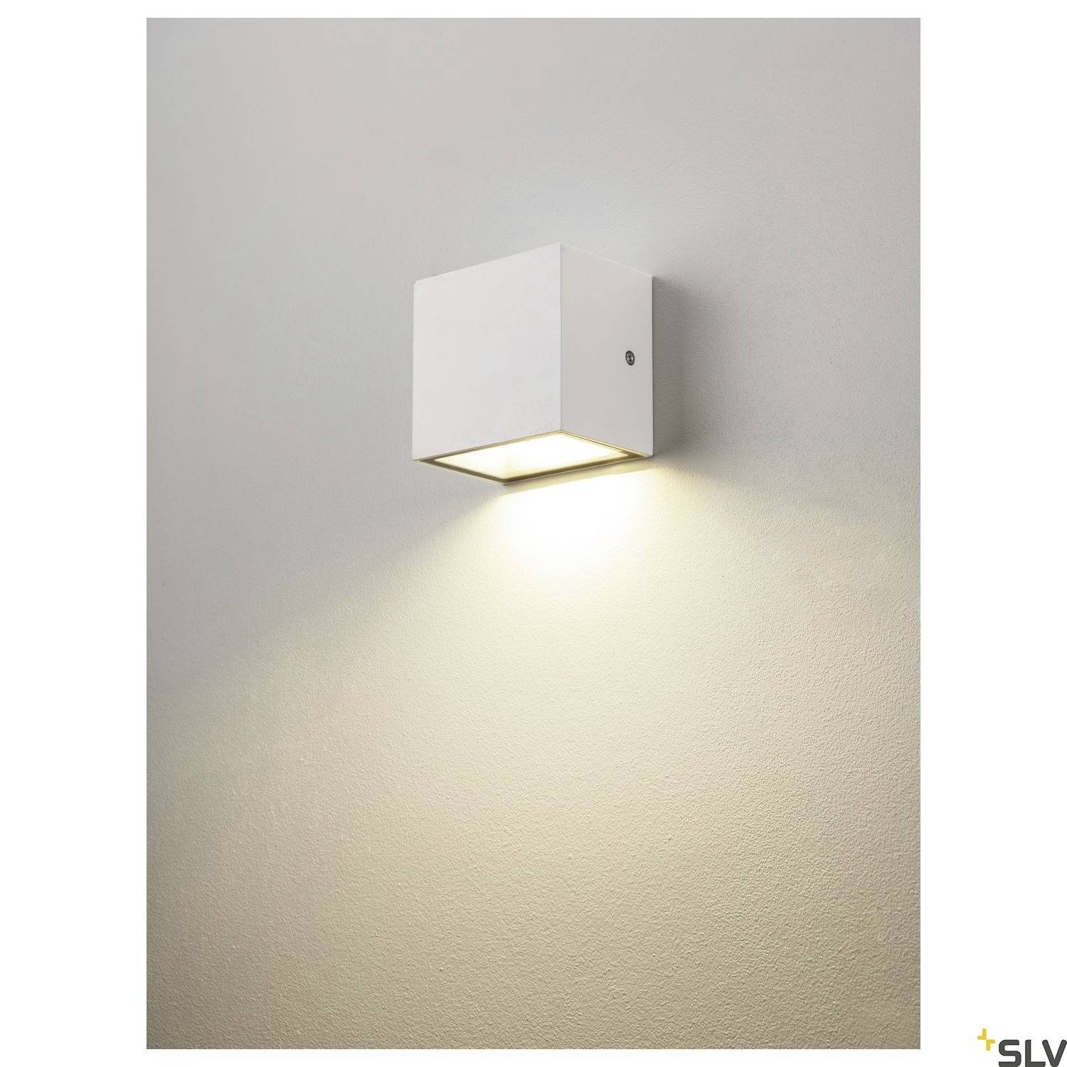 Weiße, würfelförmige Wandleuchte hängt an der Wand, strahlt Licht nach unten. Die Oberfläche der Wand wird sanft beleuchtet.