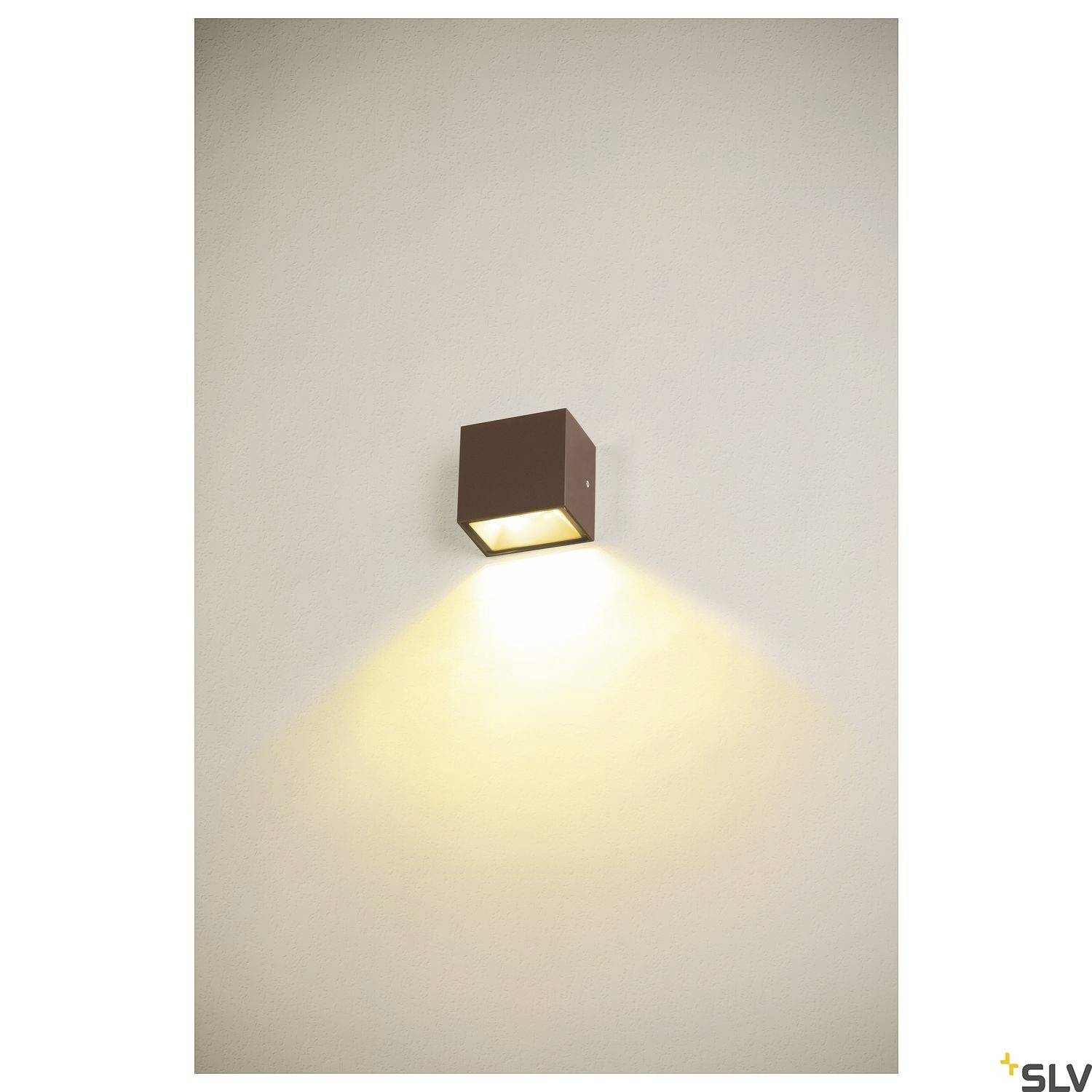 Ein quadratisches, braunes Wandleuchtmodul strahlt warmes Licht auf eine beige Wand.