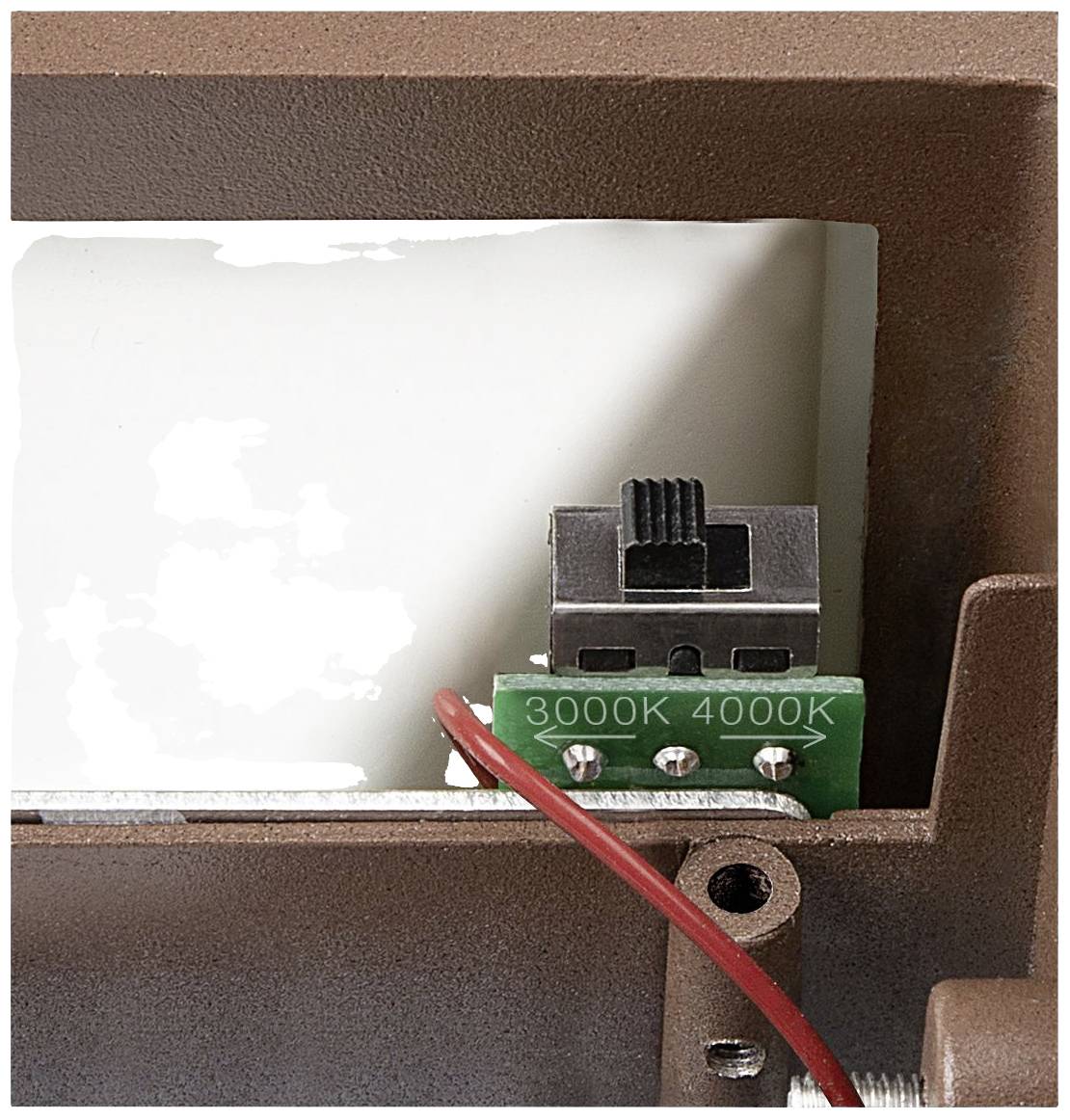 Ein Schalter mit zwei Positionen '3000K' und '4000K' ist auf einer Leiterplatte in einem metallischen Gehäuse montiert, neben einem roten Kabel.