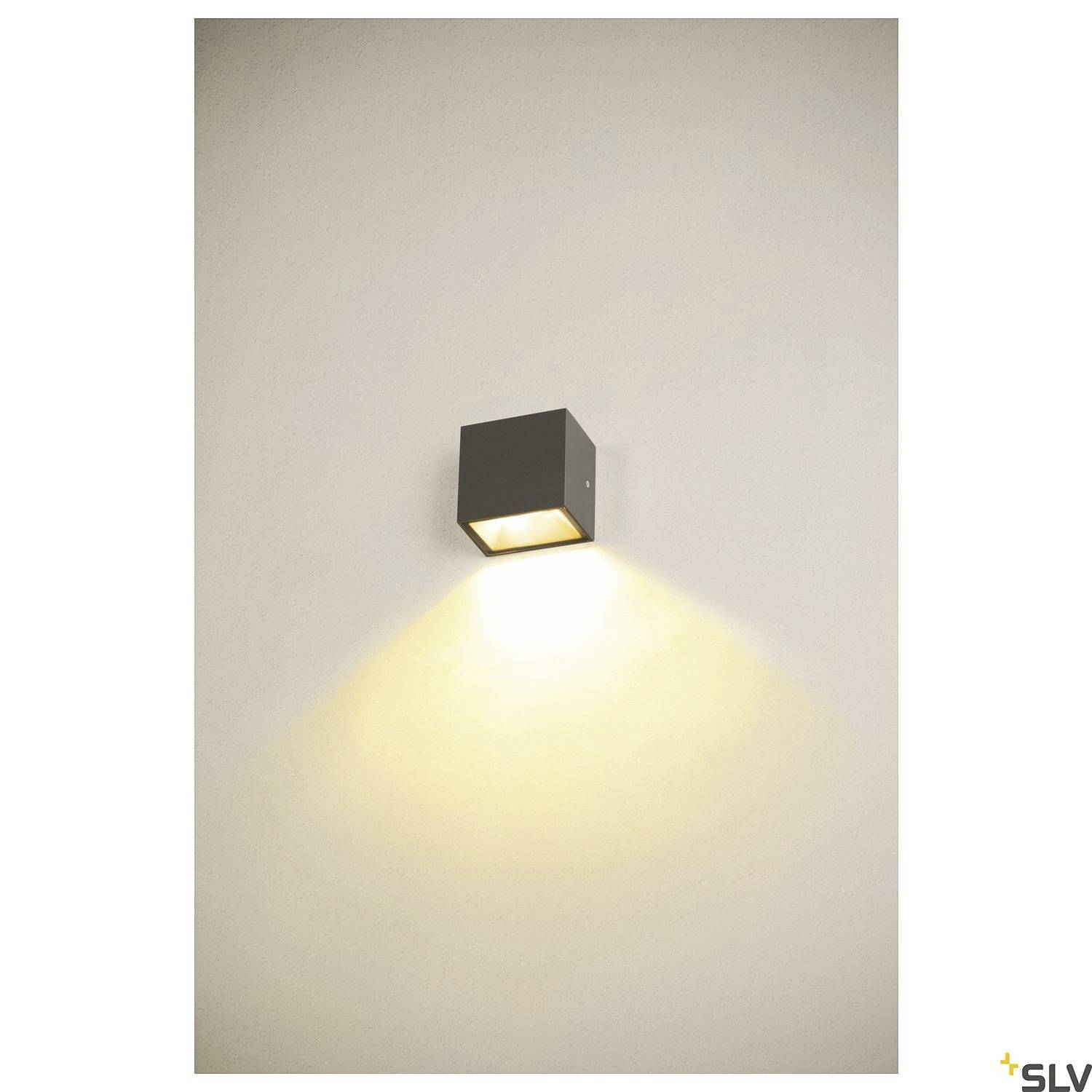Wandleuchte mit schlichtem, modernem Design. Eine quadratische Lampe strahlt warmes Licht nach unten, erzeugt dezente Beleuchtung.