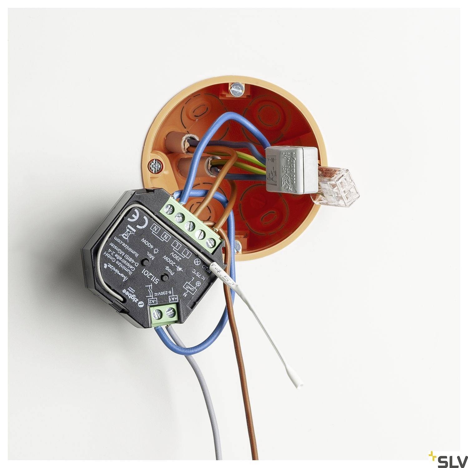 Eine offene runde Steckdose zeigt mehrere bunte Kabel und angeschlossene elektrische Komponenten, die in die Wand integriert sind.