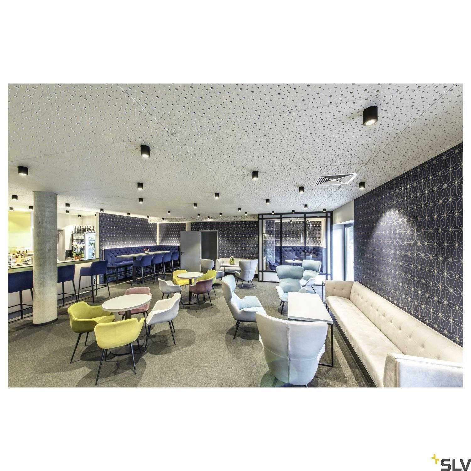 Gemütlicher Loungebereich mit moderner Inneneinrichtung, farbigen Stühlen und Sofas, dezent beleuchtet mit zahlreichen Deckenleuchten.