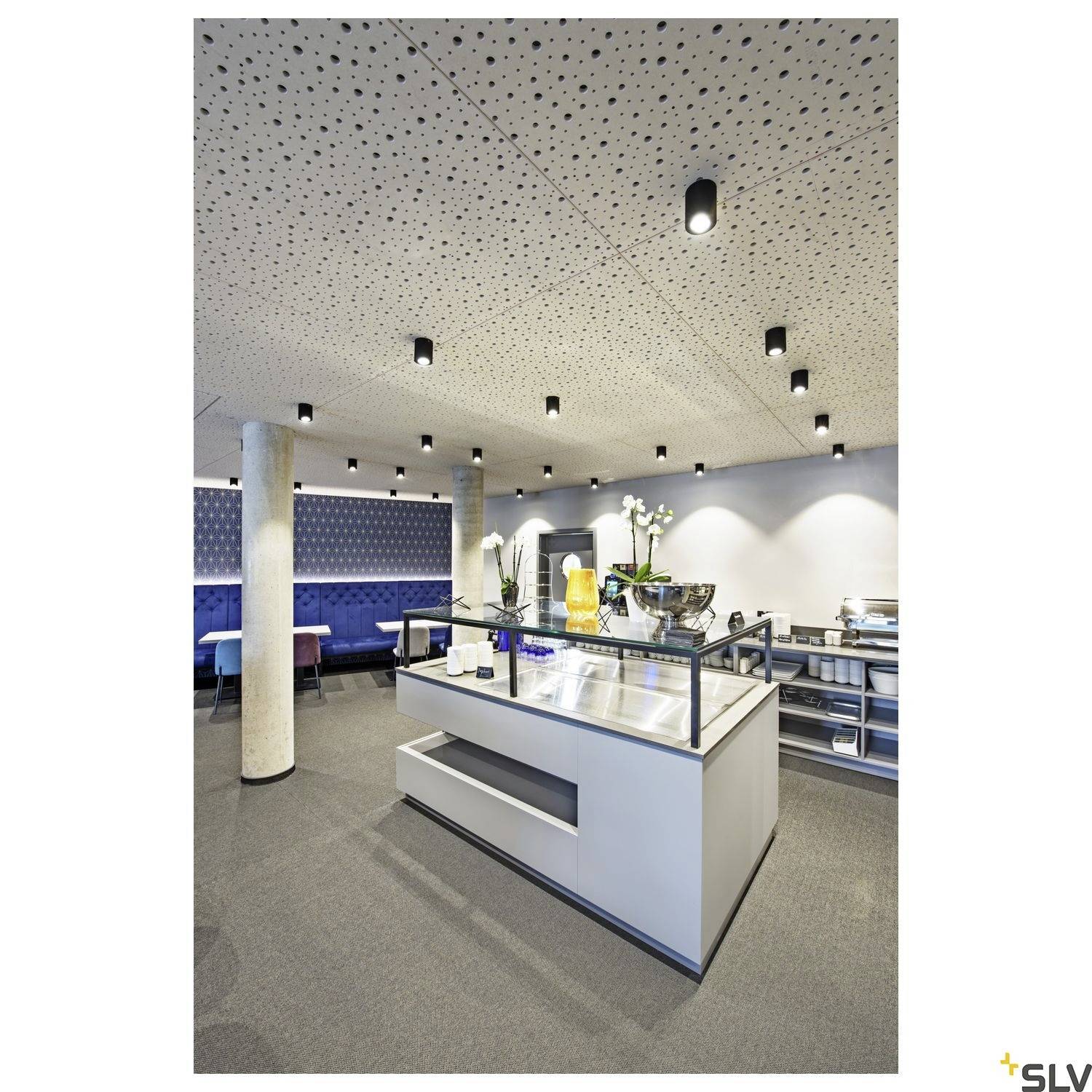 Eine moderne Kantine mit LED-Deckenspots, die helles Licht auf Tische und einen Buffetbereich werfen. Sitzgelegenheiten im Hintergrund.