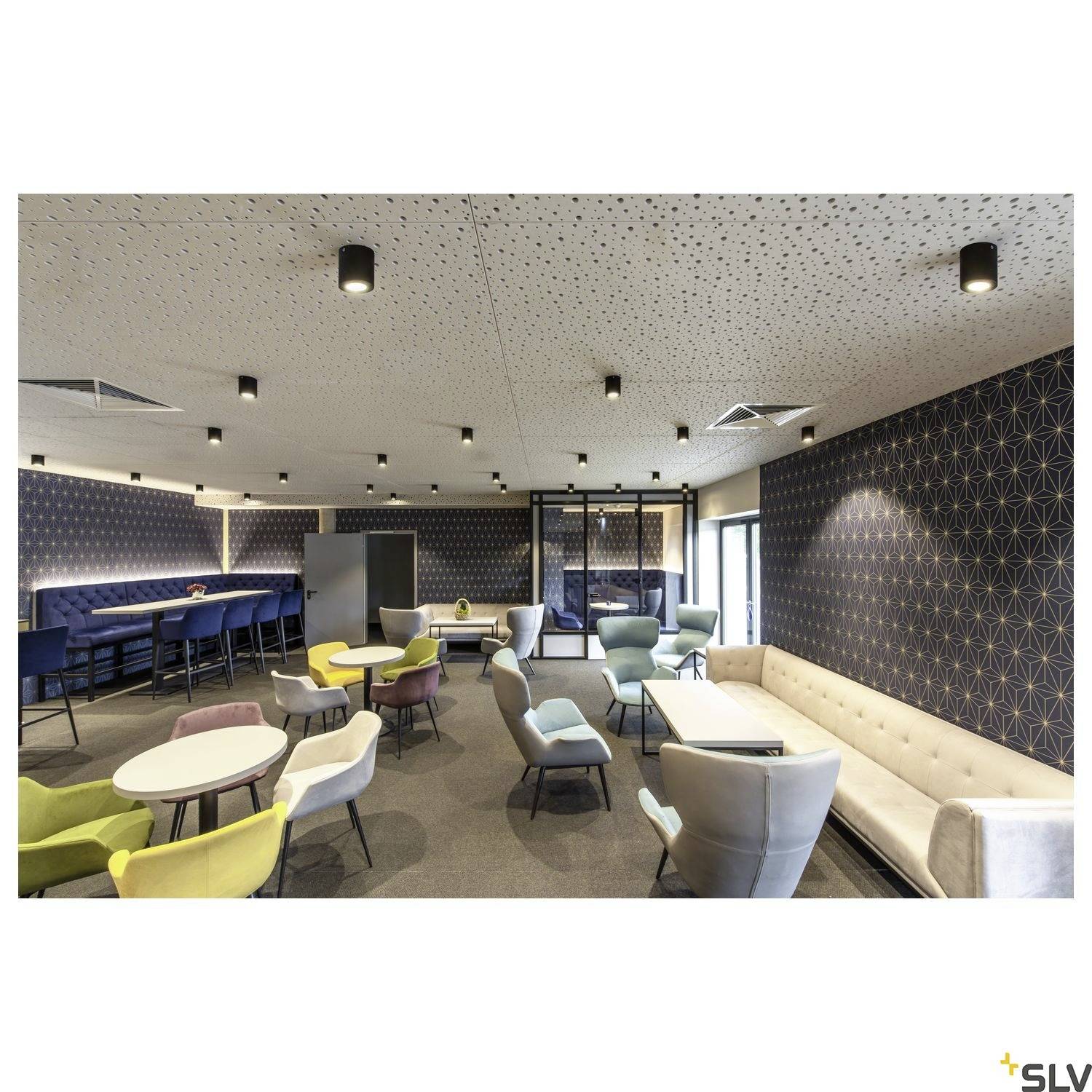 Ein modern gestalteter Raum mit farbenfrohen Sesseln, Tischen und einer Loungeecke. Die Decke ist mit zahlreichen Downlights beleuchtet.