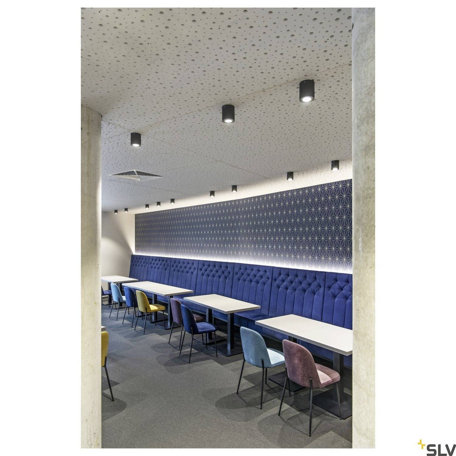 Ein modern eingerichteter Raum mit bunten Stühlen, blauer gepolsterter Bank an der Wand und schlichter Beleuchtung an der Decke.