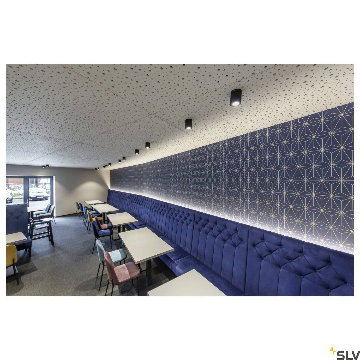 Moderne Cafeteria mit blauen gepolsterten Sitzbänken und mehreren Tischen. Die Decke ist mit kleinen schwarzen Leuchten versehen.