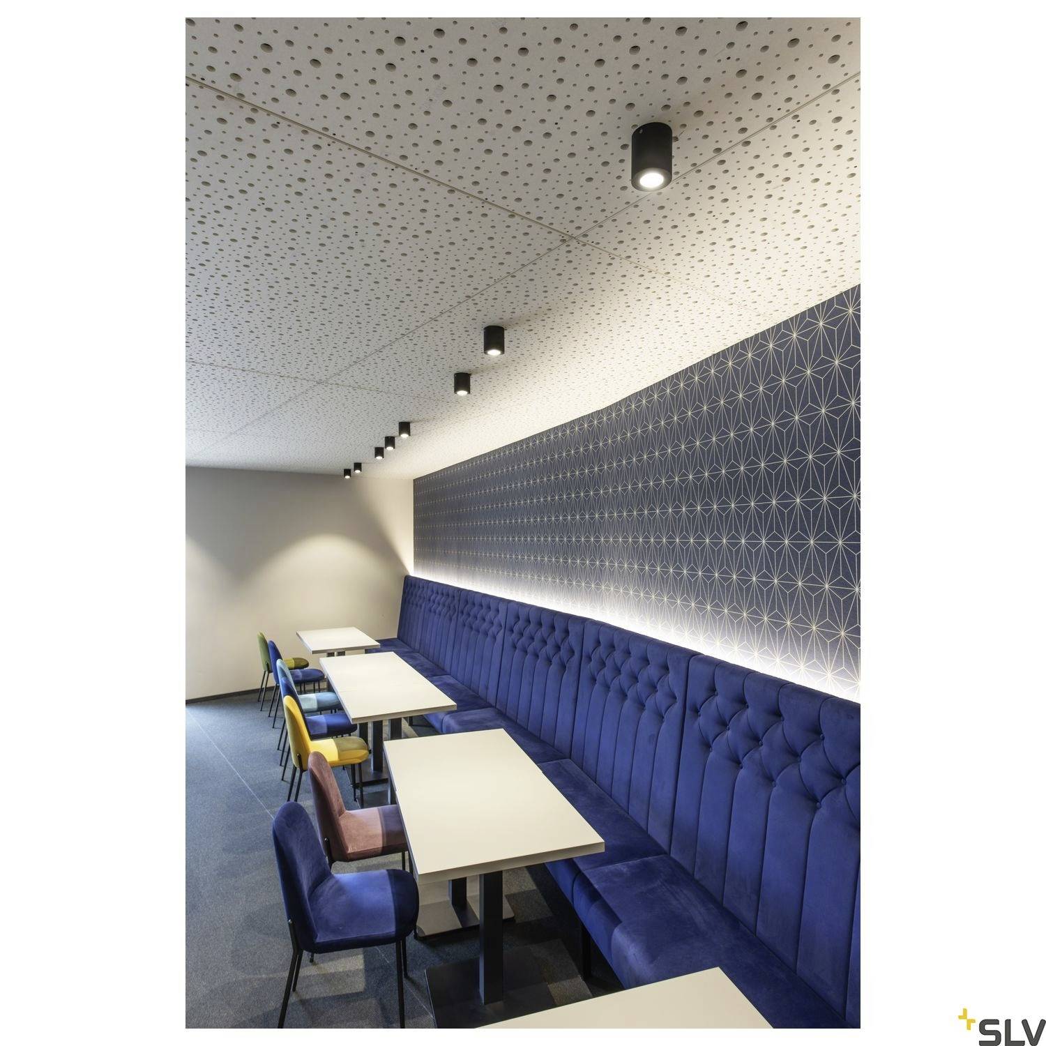 Moderne Innenansicht eines Cafés mit blauen Sitzbänken, geometrisch gemusterter Tapete und einer Reihe von Tischen mit bunten Stühlen.