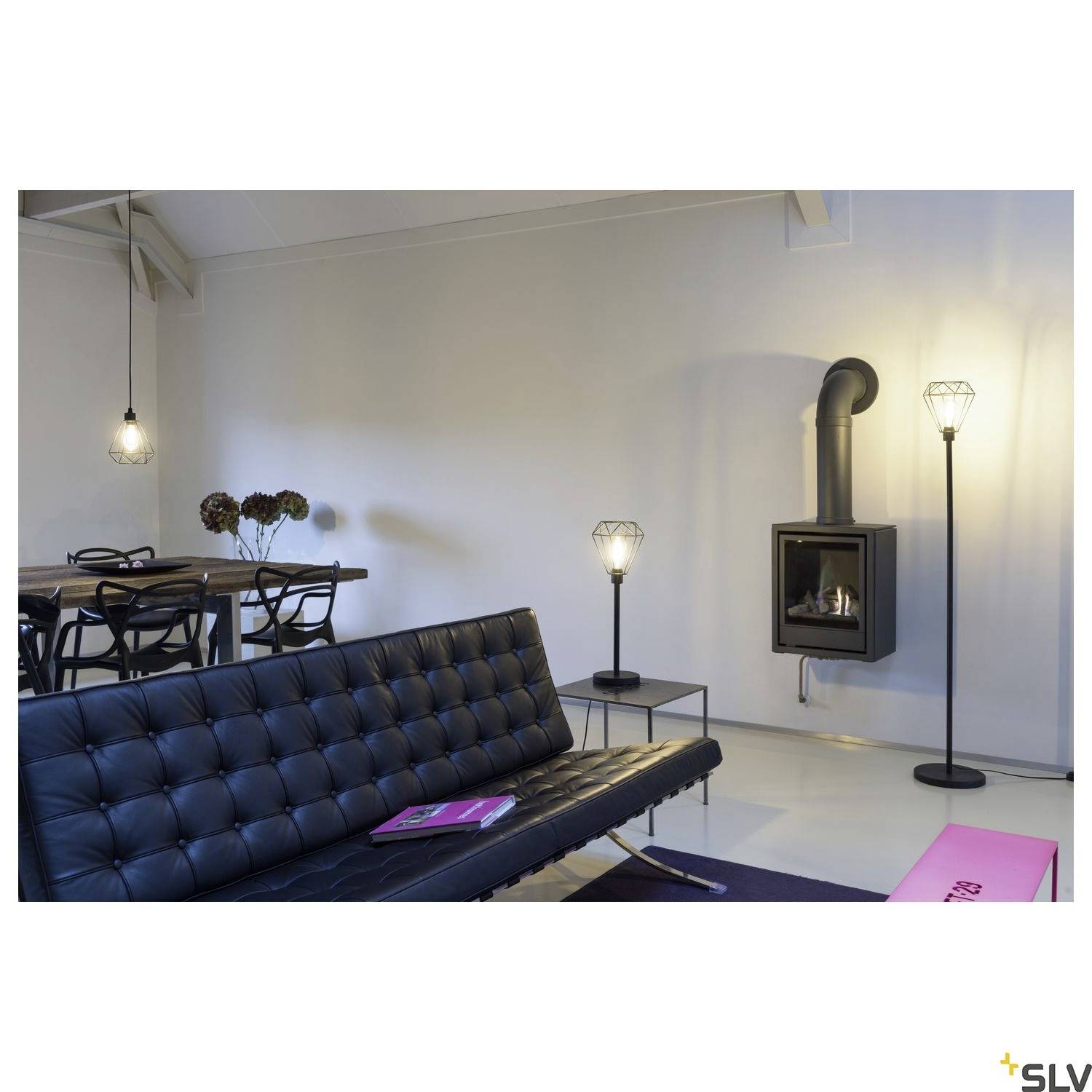 Ein modernes Wohnzimmer mit einem schwarzen Sofa, einem Holztisch mit Stühlen und einem an der Wand angebrachten Kamin.