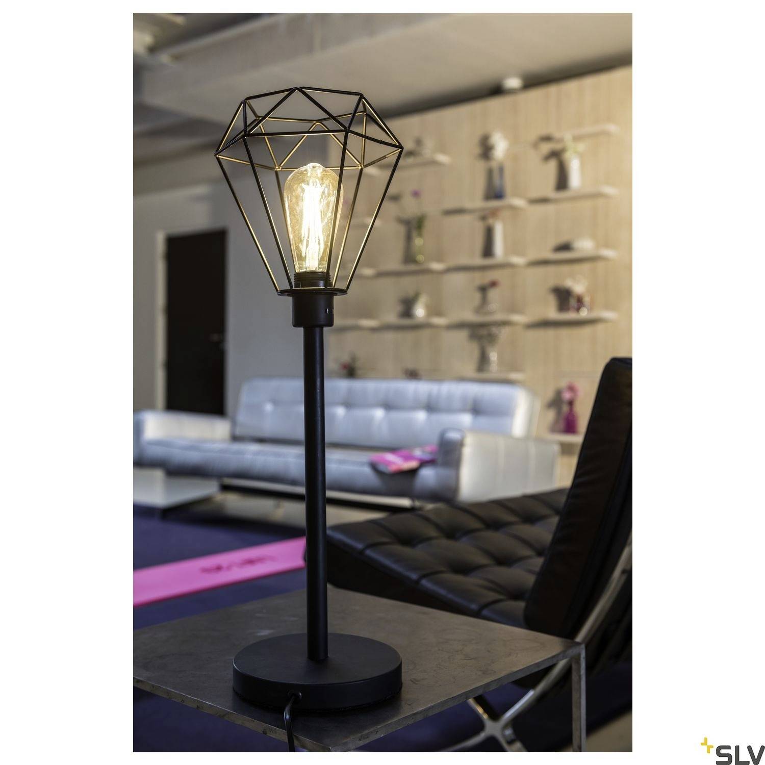 Schwarz-goldene Tischlampe mit geometrischem Drahtgestell und Glühbirne leuchtet in modernem, stilvollem Wohnzimmer.