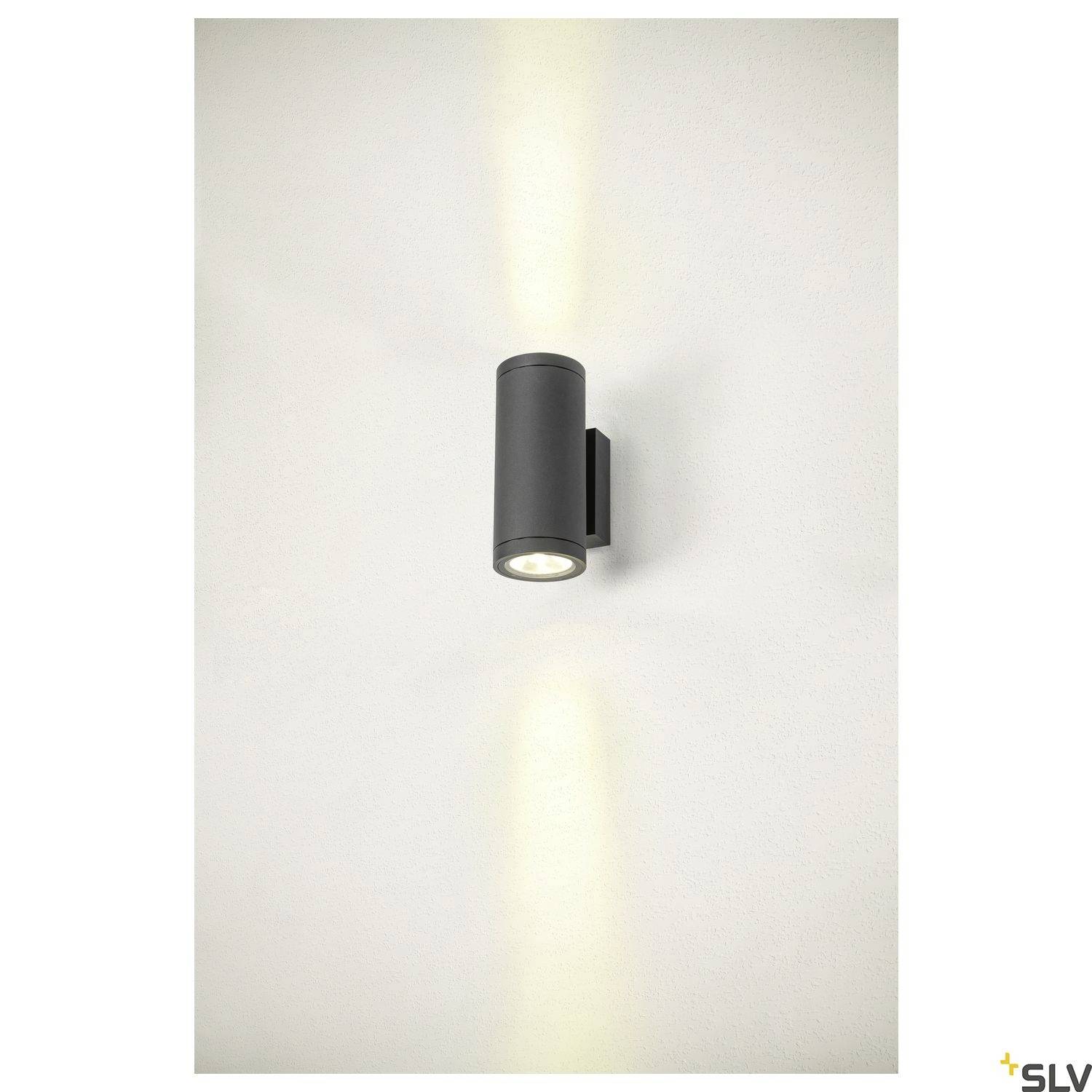 Schwarze Wandlampe mit zylindrischem Gehäuse strahlt Licht nach oben und unten aus und wirft an die Wand gerichtete Lichtkegel.