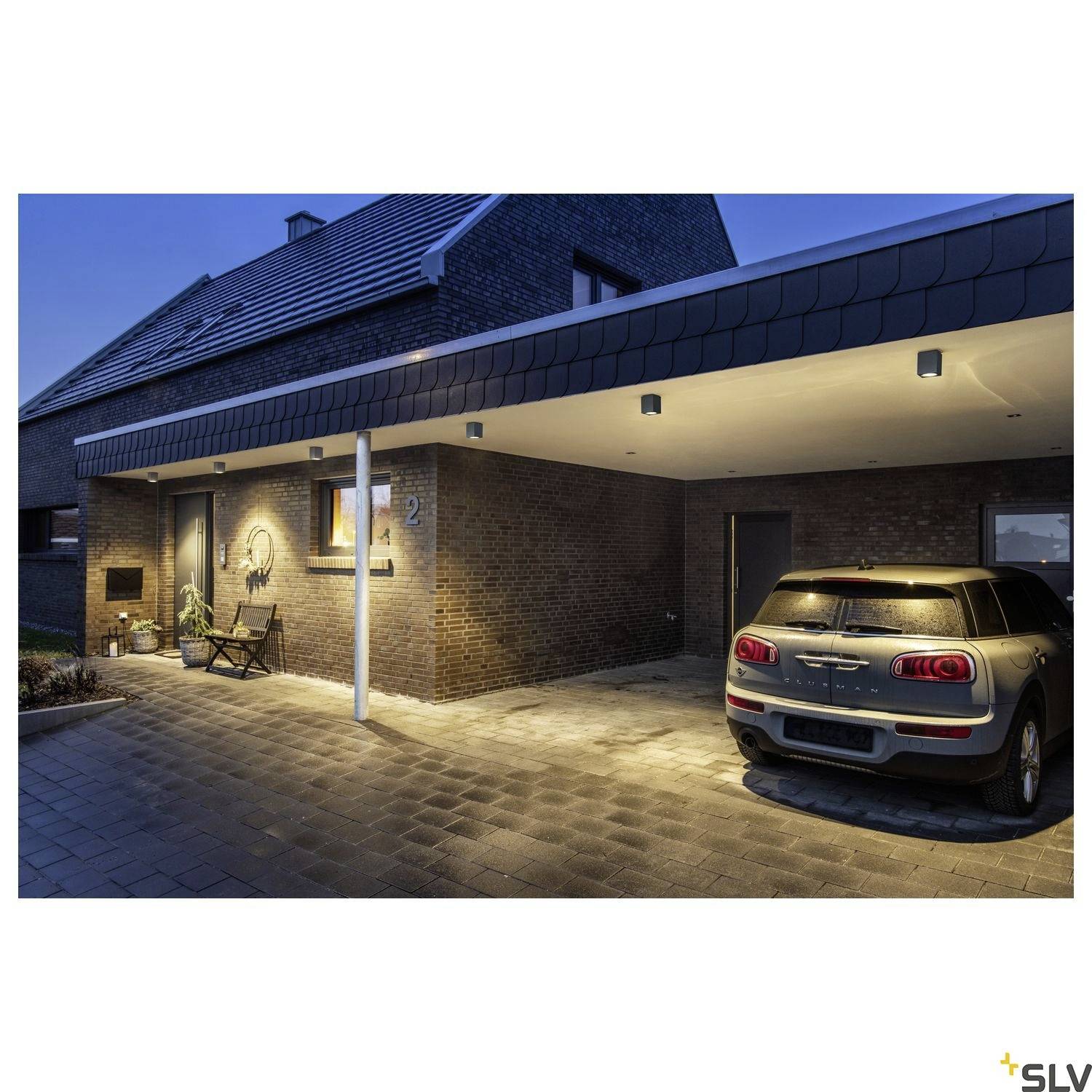 Ein modernes Einfamilienhaus bei Dämmerung, beleuchtet mit Außenleuchten. Rechts steht ein weißes Auto unter einem Carport.