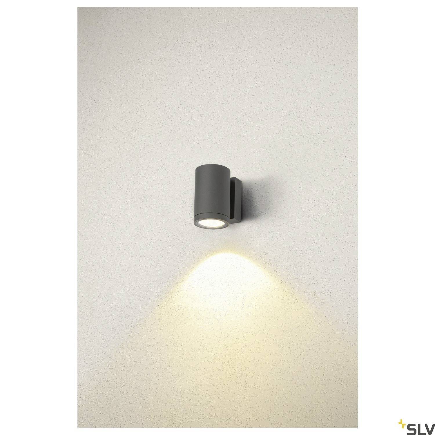 Schwarze Wandleuchte strahlt nach unten auf weiße Wand und erzeugt kegelförmigen Lichtstrahl. Dezentes, modernes Design für Innenräume.