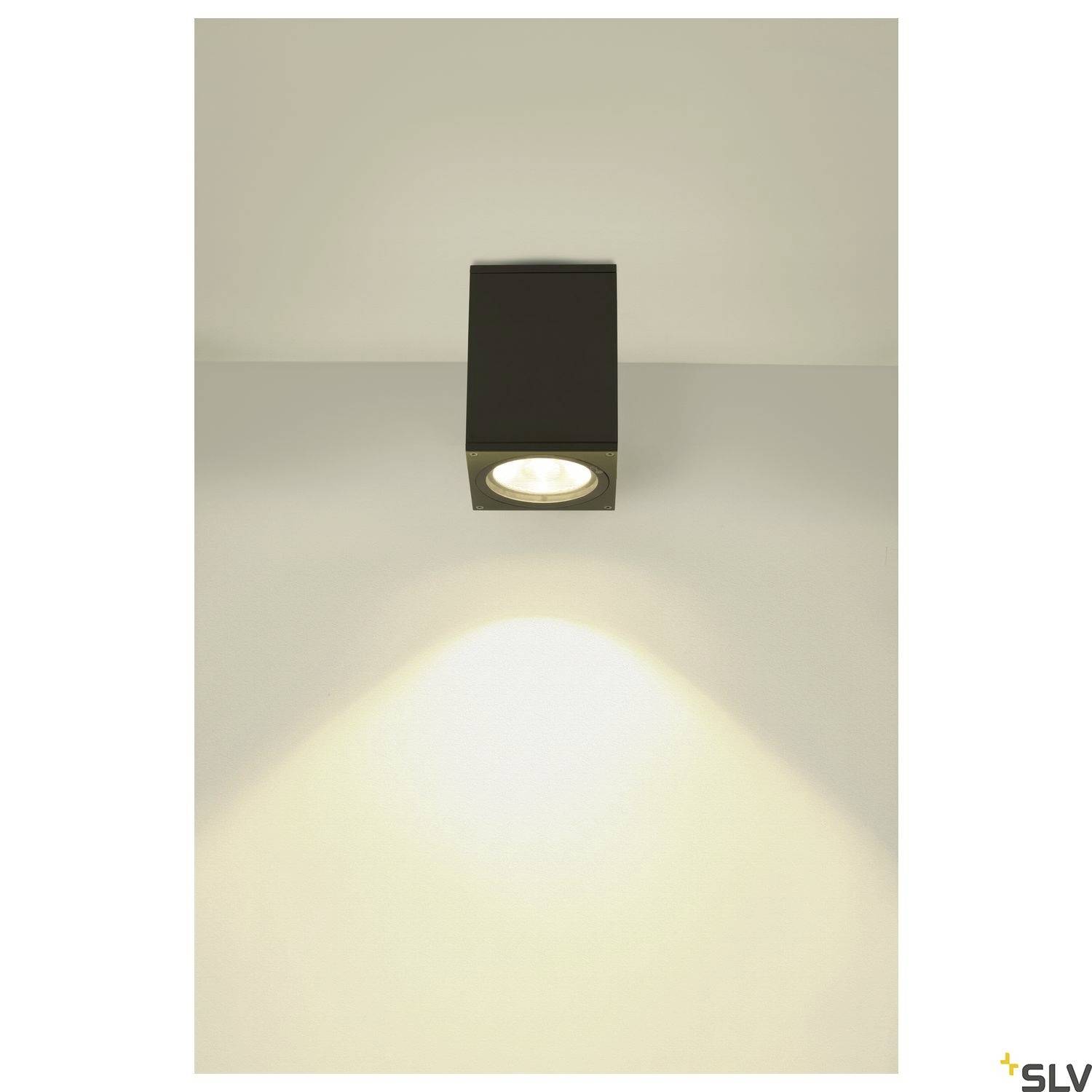 Wandleuchte mit quadratischem Gehäuse, beleuchtet eine Wand nach unten. Elegantes, minimalistisches Design mit warmem Licht.