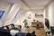 Gemütliches Wohnzimmer in einer Dachgeschosswohnung mit Sofa, Pflanzen, Schreibtisch und Fernseher. Moderne Beleuchtung an der Decke.