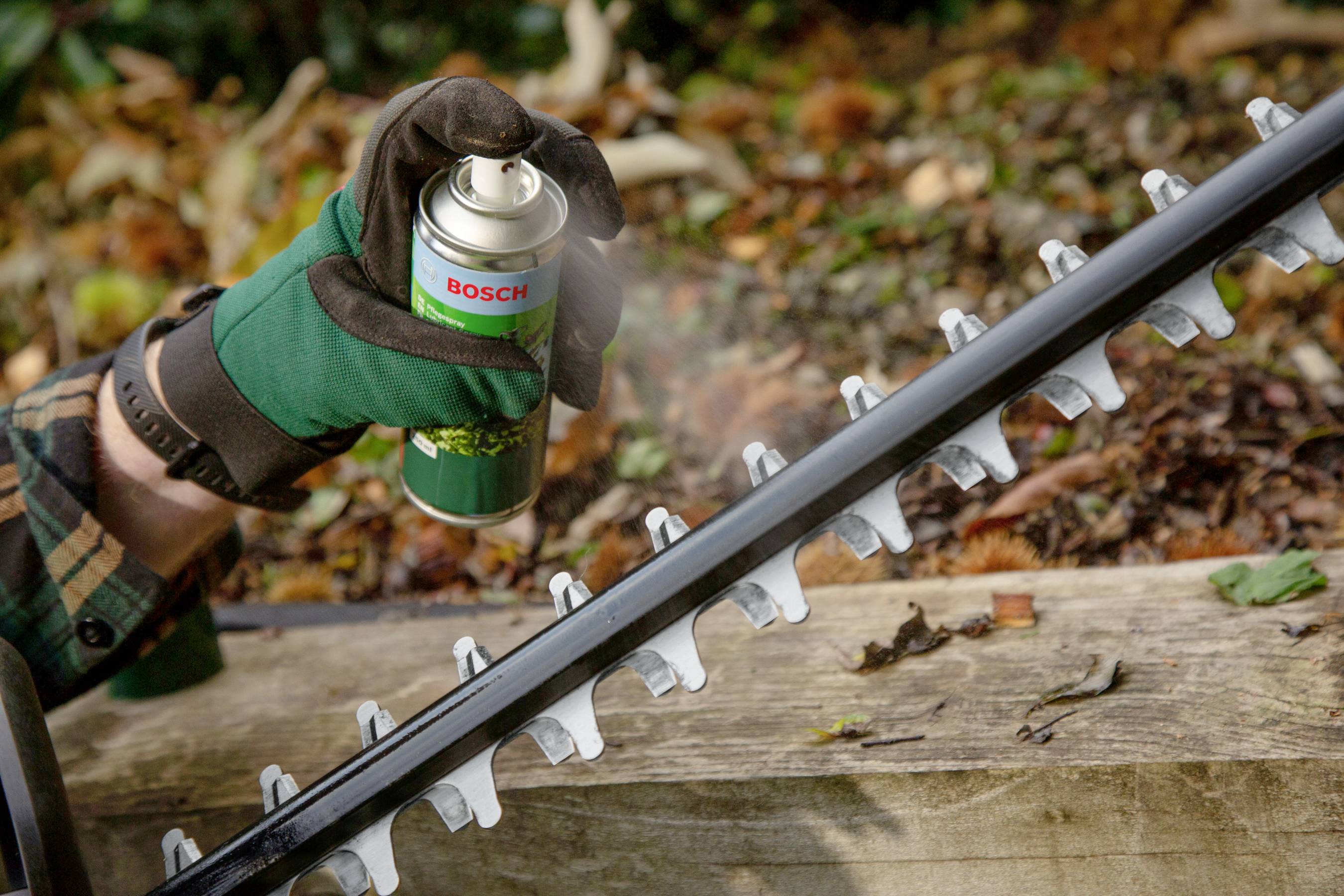 'Person sprüht Schmiermittel auf eine Heckenschere.'