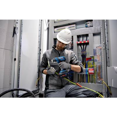 Ein Elektriker in Arbeitskleidung und Schutzhelm überprüft Kabelverbindungen in einem geöffneten Schaltschrank mit verschiedenen Kabeln und Schaltungen.