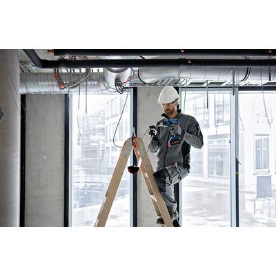 Ein Bauarbeiter steht auf einer Leiter und verwendet einen Akkubohrer, um Kabel an der Decke eines unfertigen Gebäudes zu installieren.