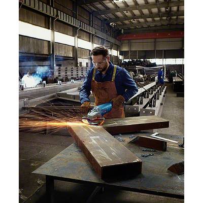 Ein Mann in einer Werkhalle schleift ein Metallstück mit einem Winkelschleifer, Funken fliegen. Arbeiter im Hintergrund, industrielle Umgebung.