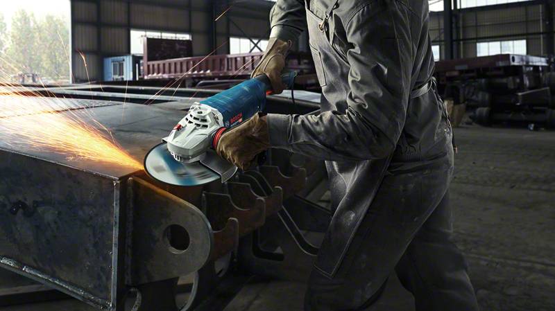 Eine Person arbeitet in einer Werkstatt mit einem Winkelschleifer und erzeugt Funken beim Schleifen von Metall.