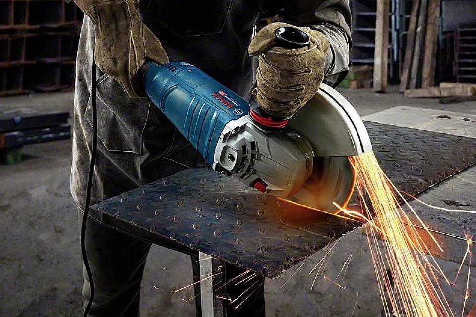 Eine Person schneidet mit einem Winkelschleifer ein Metallblech, Funken sprühen. Armlänge Handschuhe und Schutzkleidung getragen.