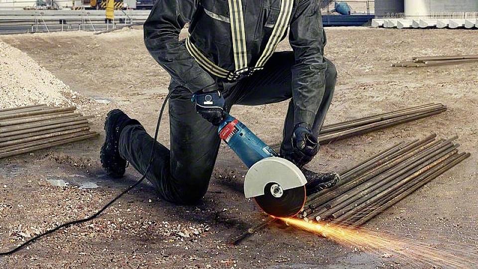 Ein Bauarbeiter schneidet mit einem Winkelschleifer Metallstäbe auf einer Baustelle. Funken sprühen vom Schneidpunkt.