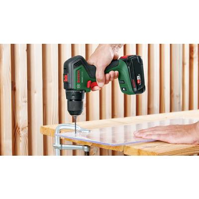 Eine Hand benutzt einen Akkubohrer, um ein Loch in eine an einer Holzwand befestigte, durchsichtige Platte zu bohren.