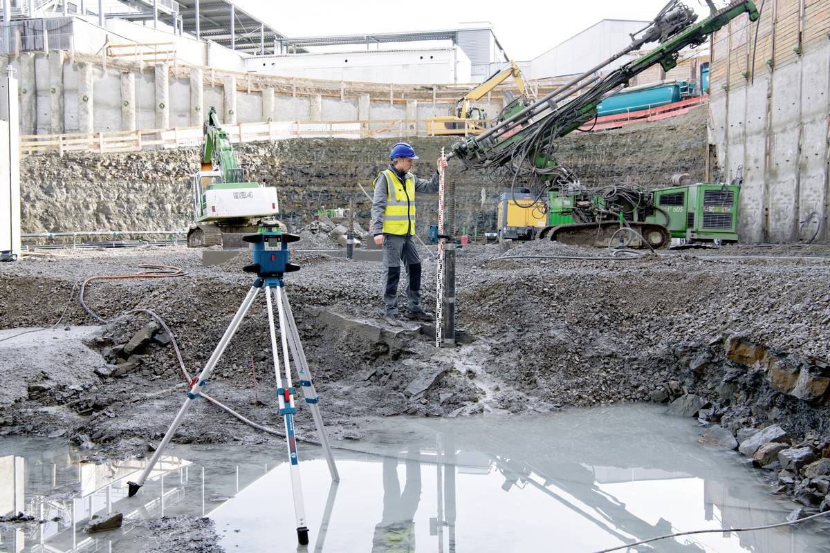 Ein Bauarbeiter in Sicherheitsweste und Helm überwacht Bohrarbeiten auf einer Baustelle mit Baugeräten und Messinstrumenten.