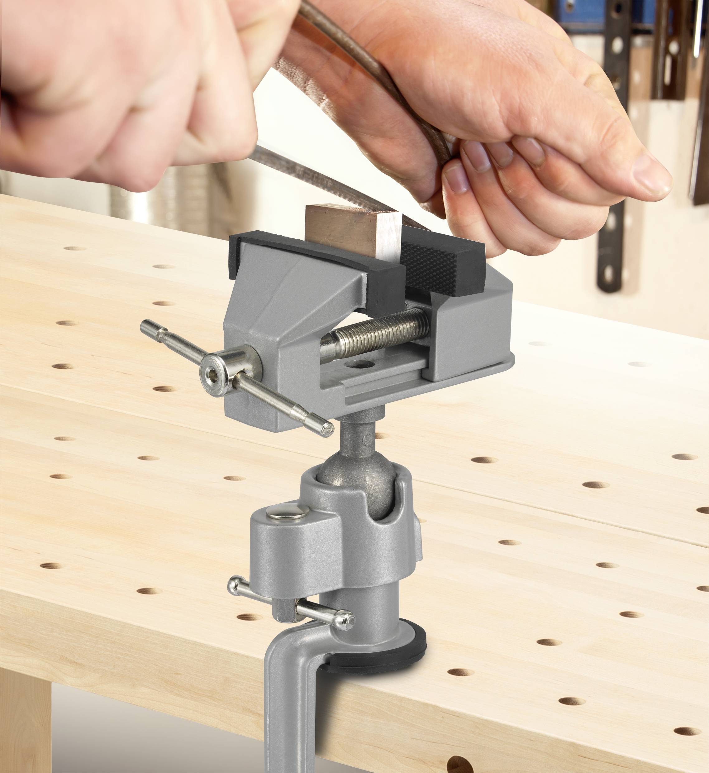 Eine Hand hält ein Metallstück in einem Schraubstock auf einer Werkbank, während eine andere Hand mit einer Feile daran arbeitet.