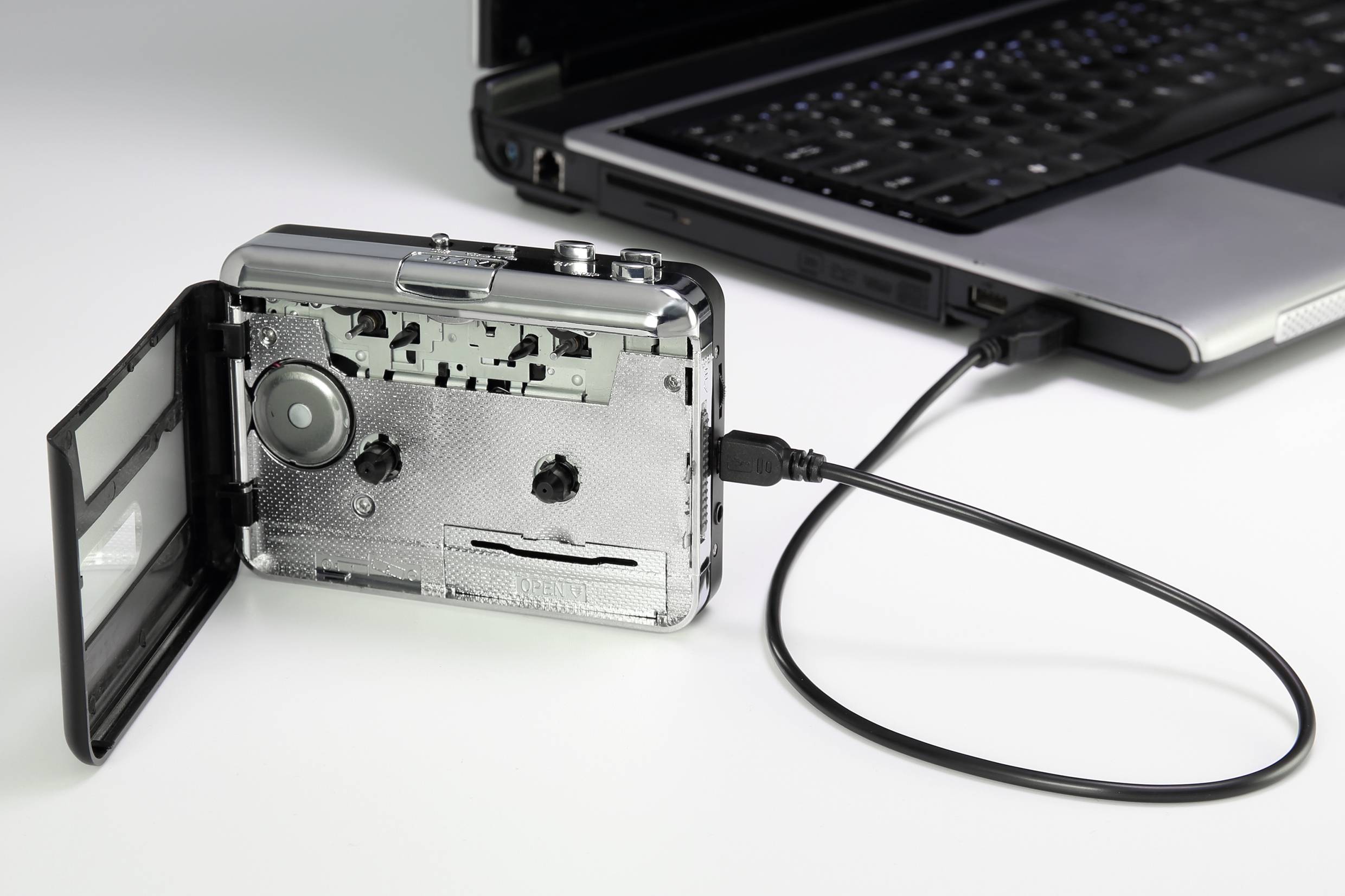 Ein Kassettenrekorder ist über ein USB-Kabel mit einem Laptop verbunden, vermutlich um Inhalte zu digitalisieren.