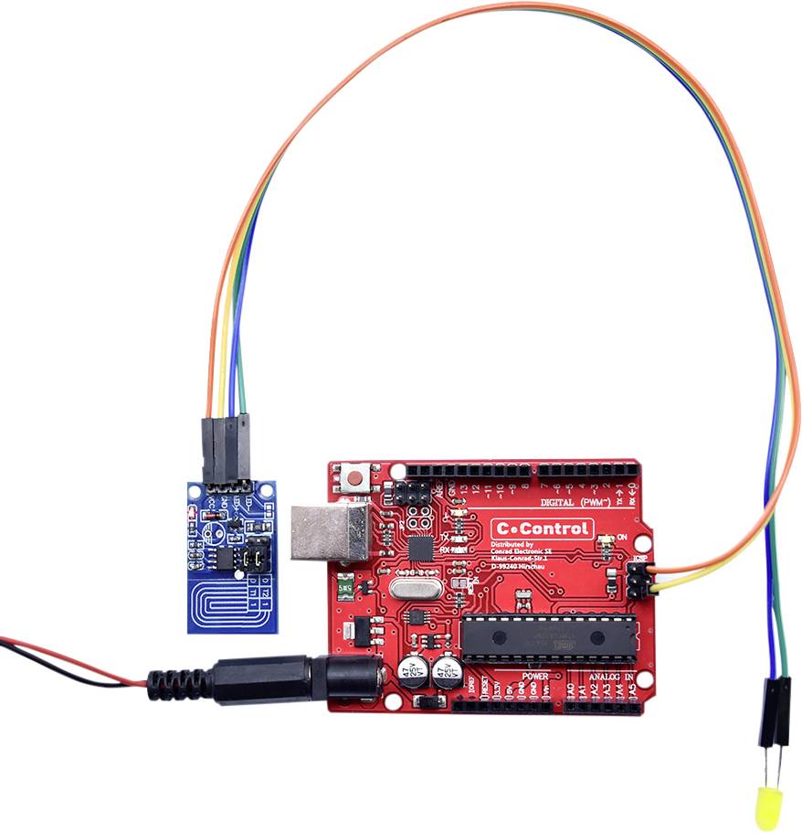Eine rote Mikrocontroller-Platine mit einem angeschlossenen blauen Sensorbauteil und Kabeln.