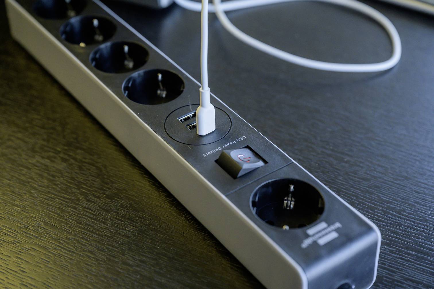 'Steckdosenleiste mit USB-Anschluss und Schalter auf einem Tisch. USB-Kabel ist eingesteckt. Digitalisierung und technische Verbindung.'