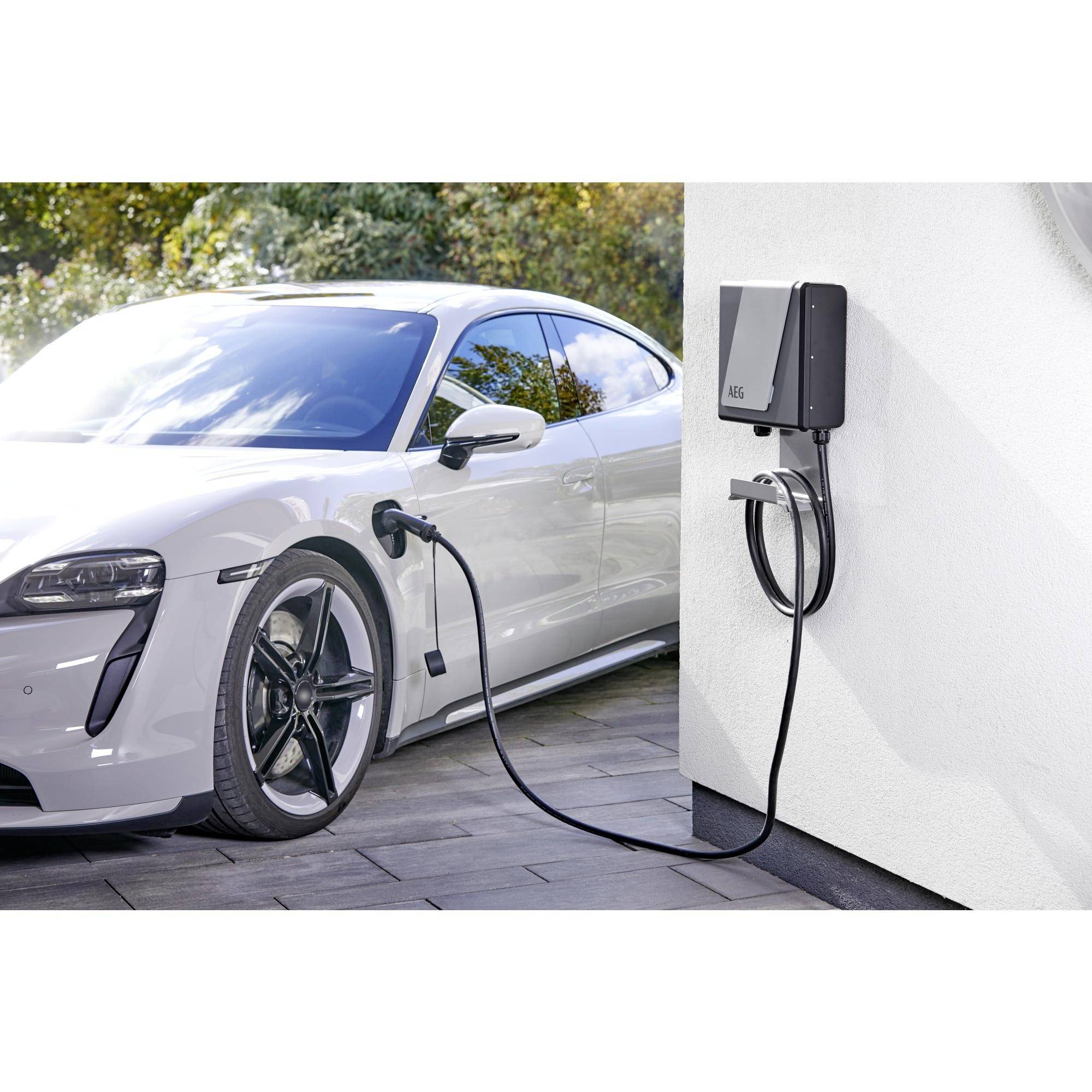 Ein weißes Elektroauto wird an einer Ladestation im Freien aufgeladen. Im Hintergrund sind Bäume und Sonnenlicht sichtbar.