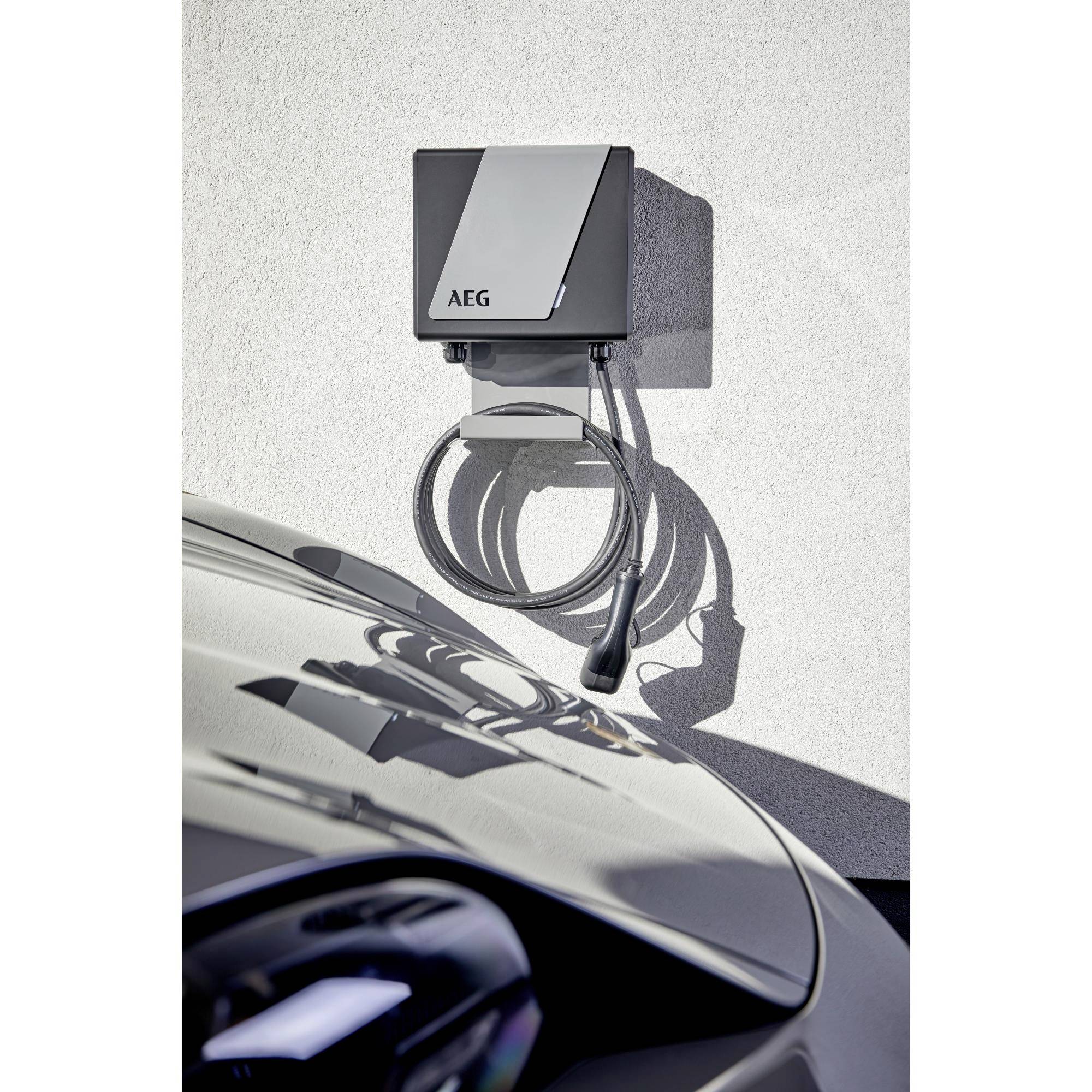 Eine elektrische Ladestation der Marke AEG ist an einer weißen Wand montiert. Ein Ladekabel hängt herab. Im Vordergrund ist ein Auto.
