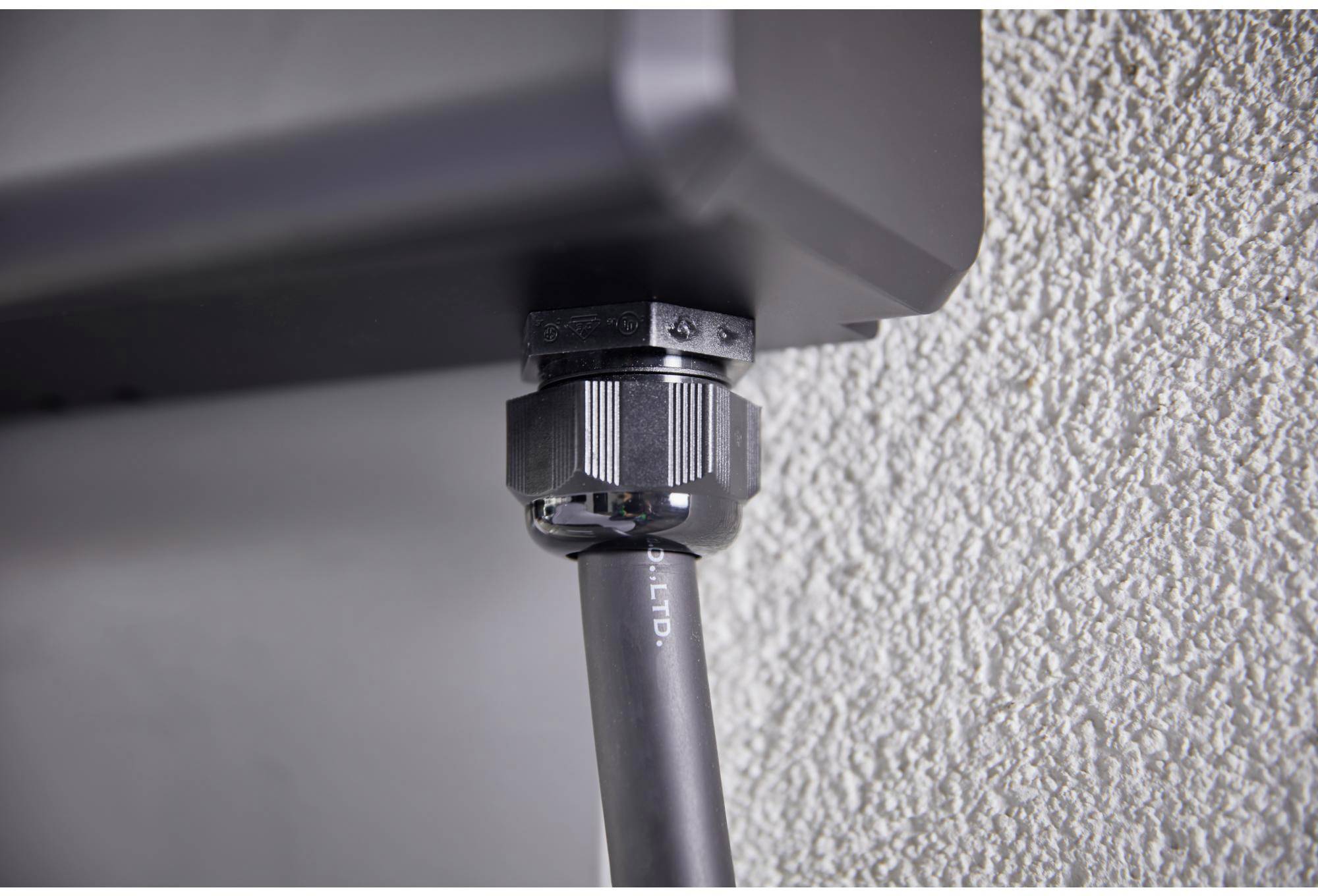 Ein Kabel aus einer wetterfesten Steckdose in einer strukturierten Wand. Die Steckdose ist sicher durch eine Verschraubung verbunden.