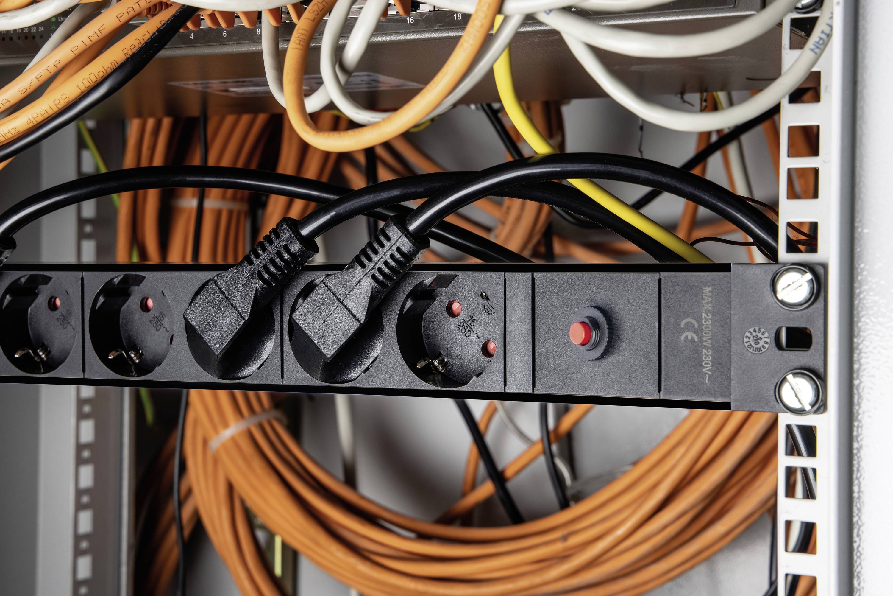 Stromverteilereinheit in einem Serverschrank mit mehreren Steckdosen und eingesteckten Kabeln. Hintergrund mit orangefarbenen und weißen Kabeln.