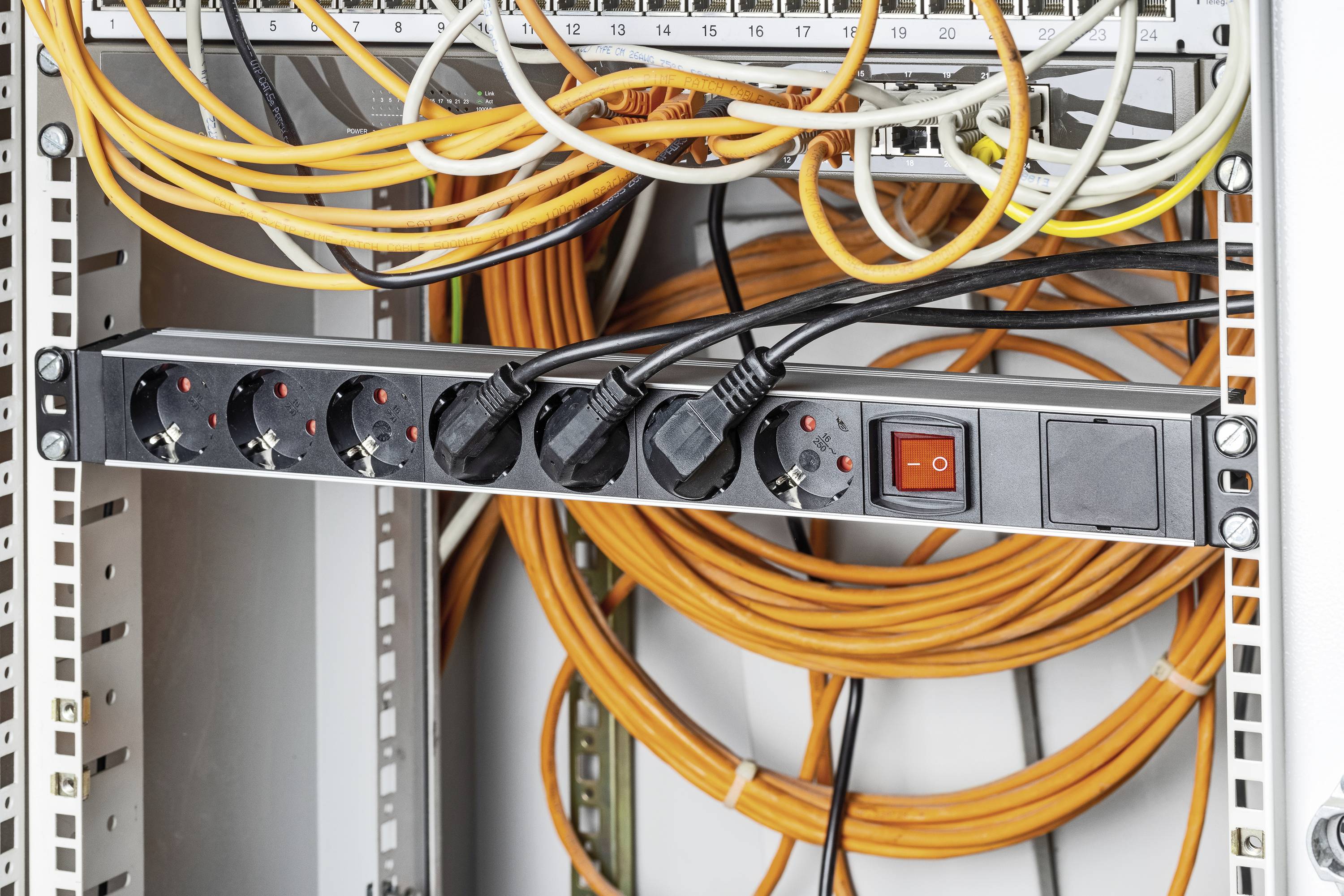 Ein Datenserverraum mit mehreren orangefarbenen und schwarzen Kabeln, die an eine Steckdosenleiste angeschlossen sind.
