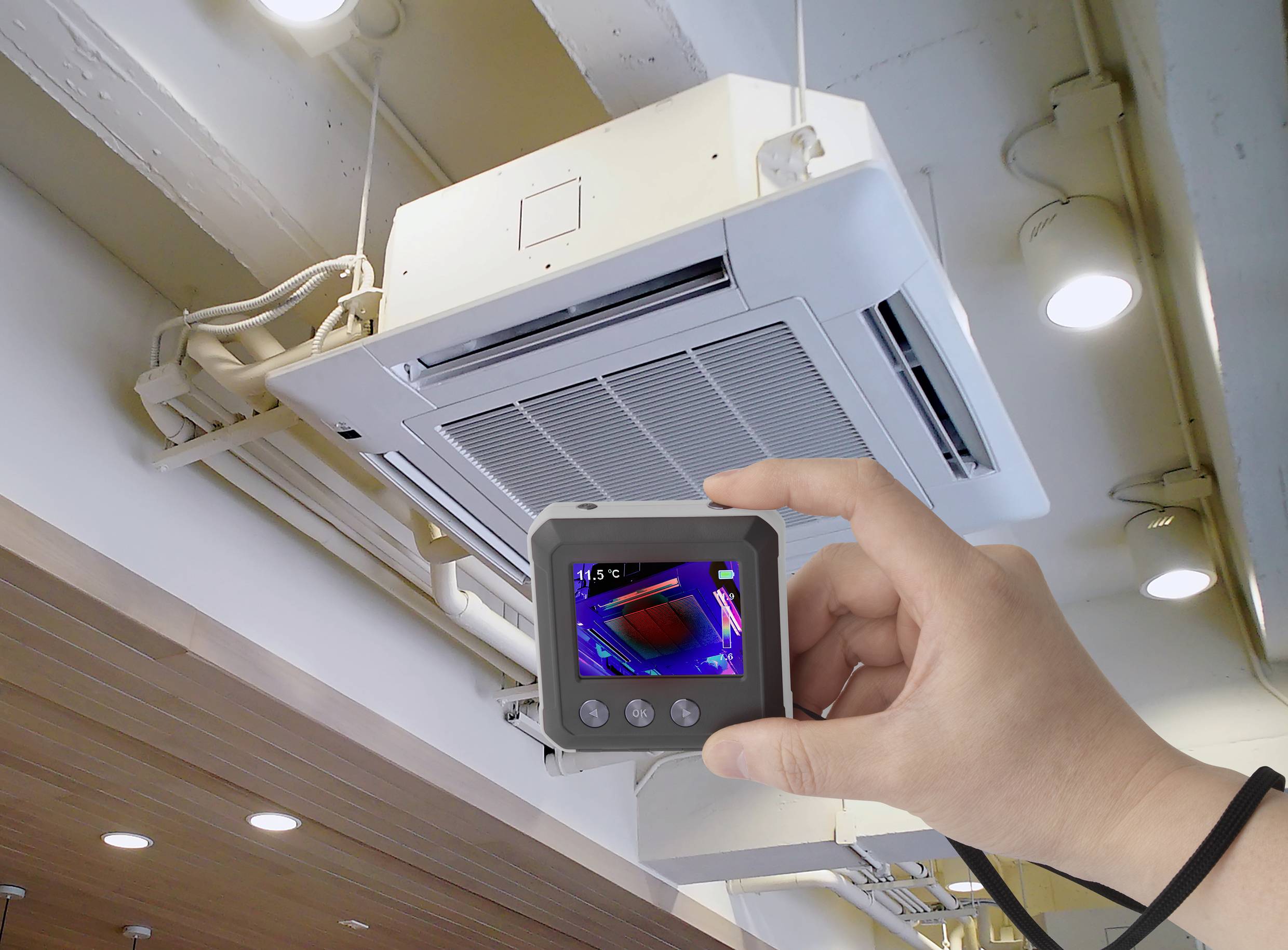 'Eine Hand hält eine Wärmebildkamera, die auf eine Klimaanlage an der Decke gerichtet ist. Die Kamera zeigt ein Wärmebild des Geräts.'