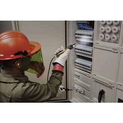Ein Elektriker mit Schutzhelm und -brille arbeitet mit einem Testgerät an einem offenen Schaltschrank voller Kabel und Sicherungen.
