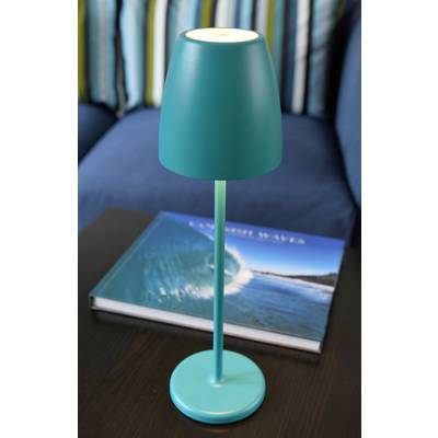 Eine türkisfarbene Tischlampe steht auf einem dunklen Holztisch. Daneben liegt ein Buch mit dem Titel 'Crashing Waves', das ein Meerbild zeigt.