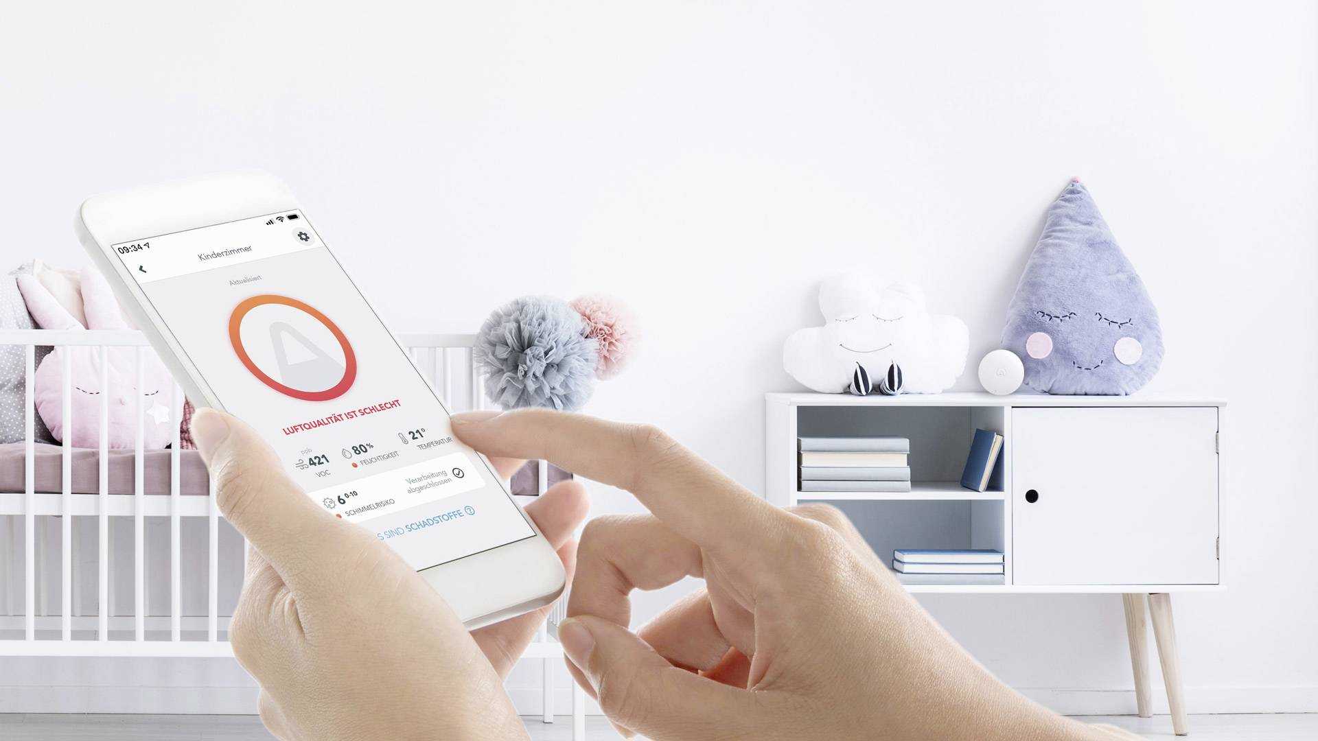Eine Person hält ein Smartphone mit einer App zur Überwachung der Raumluftqualität. Im Hintergrund ist ein Kinderzimmer zu sehen.