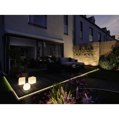 Eine moderne Terrasse bei Dämmerung, mit Sitzmöbeln, beleuchteten Würfelleuchten und Pflanzen, angrenzend an ein Wohnhaus.