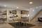 Ein modernes Wohnzimmer mit Esstisch und Stühlen, angrenzender Küche, Treppe rechts. Kunst an der Wand und moderne Beleuchtung.