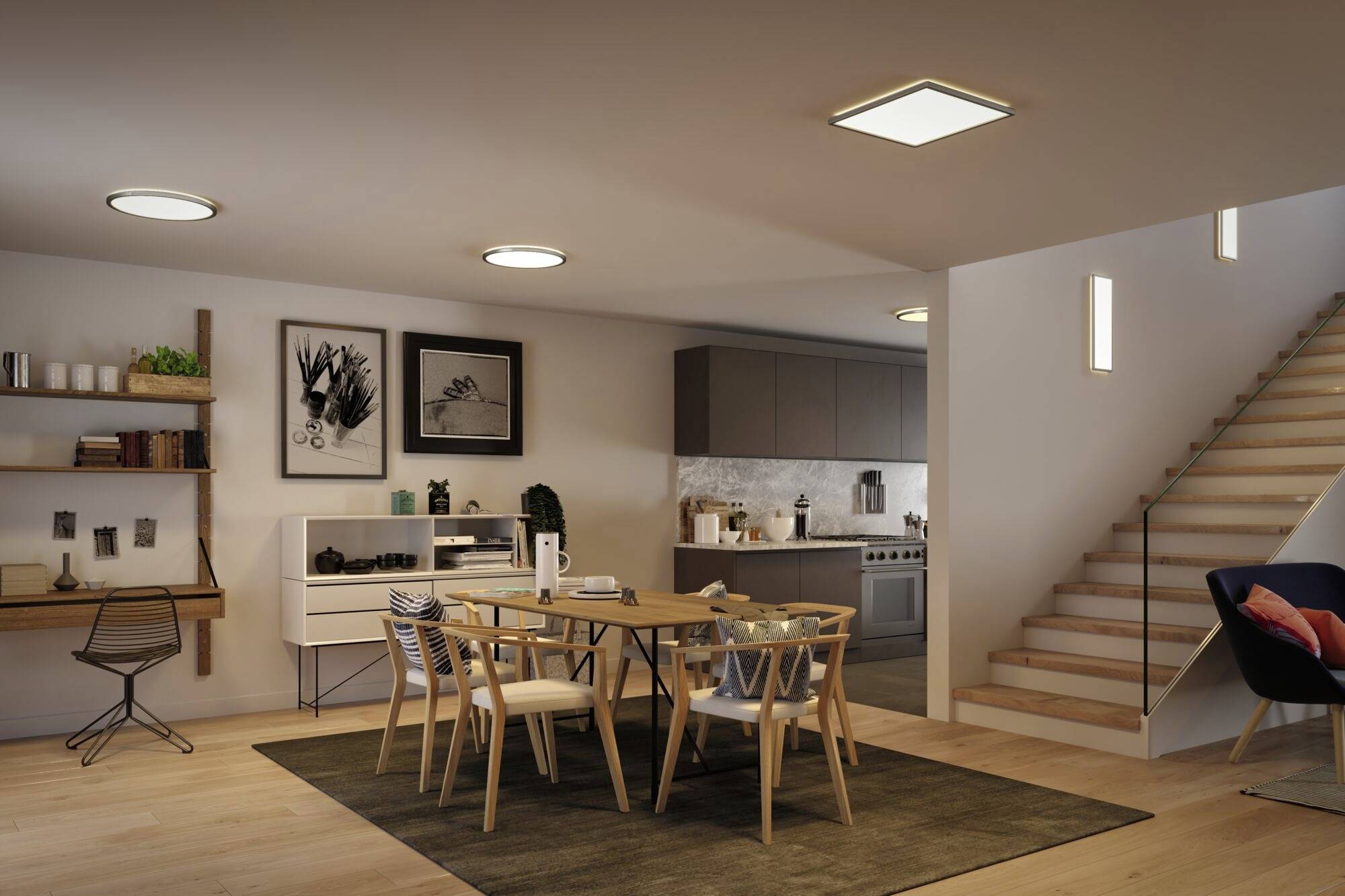Ein modern eingerichtetes Wohnzimmer mit Esstisch, Stühlen, Treppe und offener Küche. An der Wand hängen Bilder und Regale.