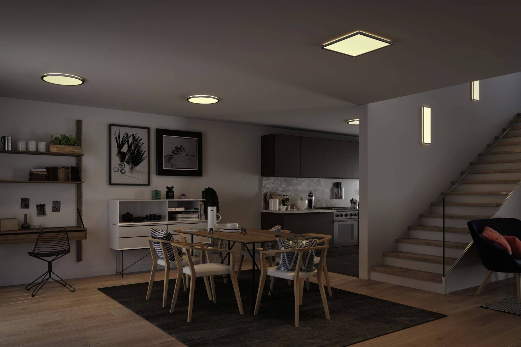 Modernes Esszimmer mit Holztisch und Stühlen. Im Hintergrund Küche mit Arbeitsplatten, rechts Treppe mit Beleuchtung. Dezente Wanddekoration.