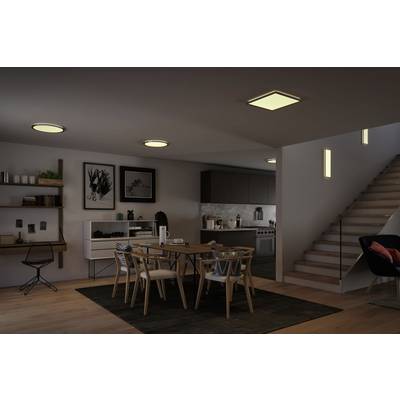 Modernes Esszimmer mit Holztisch und Stühlen. Im Hintergrund Küche mit Arbeitsplatten, rechts Treppe mit Beleuchtung. Dezente Wanddekoration.