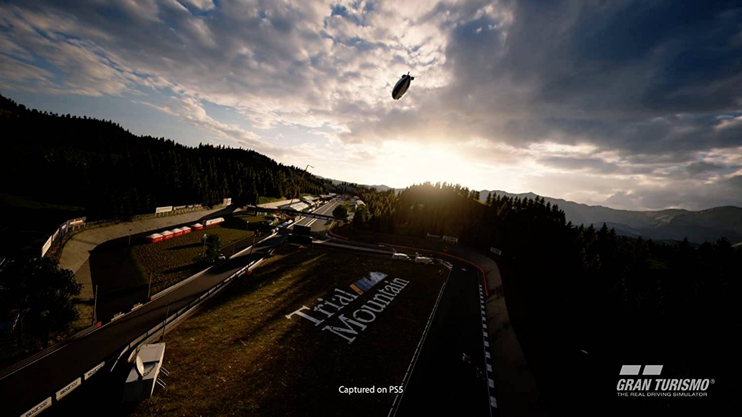 Ein Rennwagen fliegt über die Strecke in einer dramatischen Landschaft bei Sonnenuntergang. Auf der Strecke steht 'Trial Mountain'.