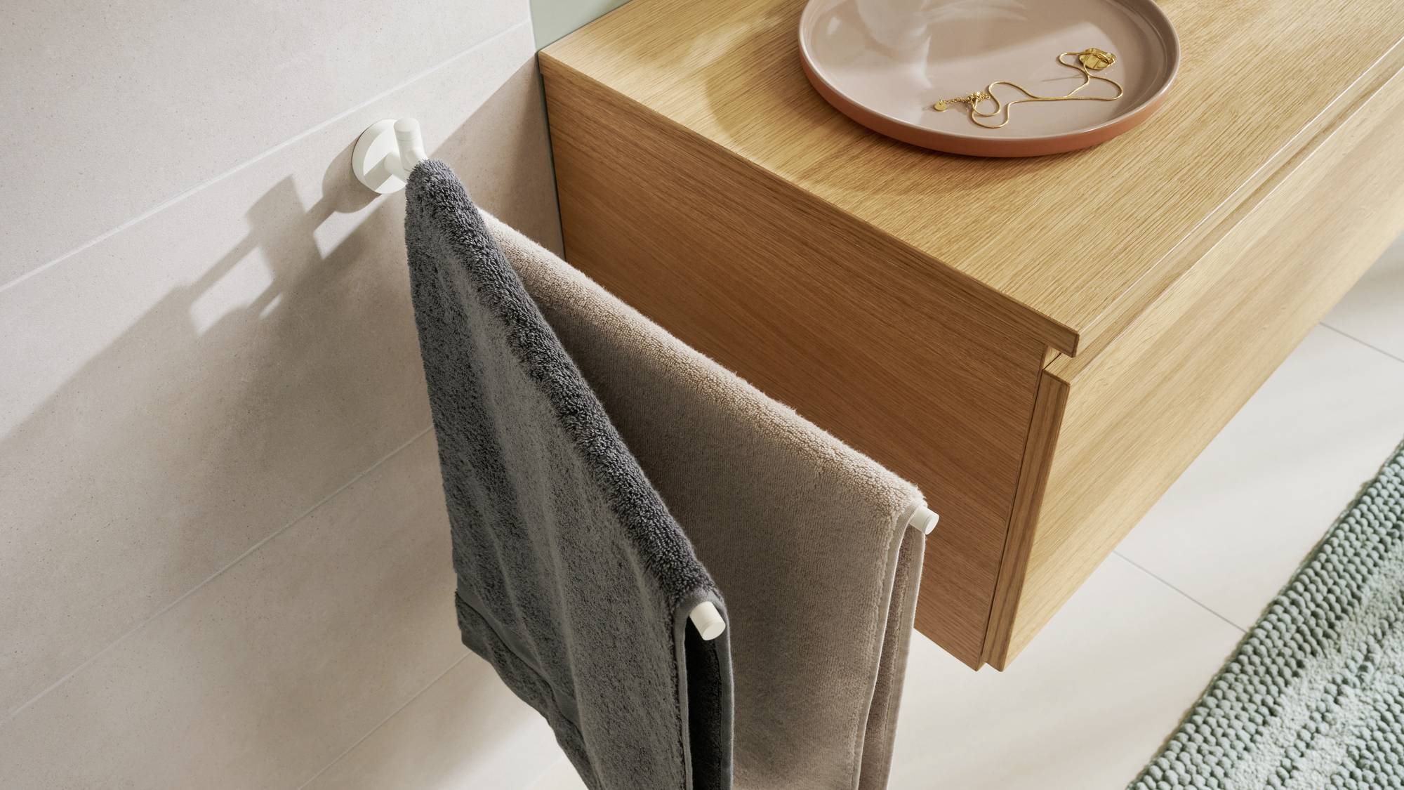 Zwei Handtücher hängen an einem Handtuchhalter neben einem Holzmöbel mit einem dekorativen Teller darauf.